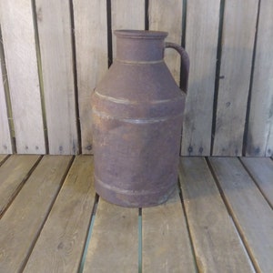May include: A rusty metal milk jug with a handle. The jug is sitting on a wooden surface.