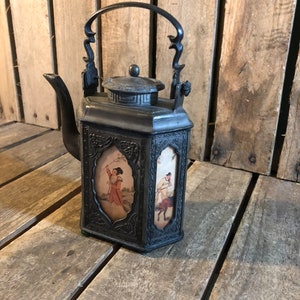 May include: A black cast iron teapot with a decorative handle and lid. The teapot has a square body with four panels, each featuring a painted scene of people in traditional Chinese clothing.
