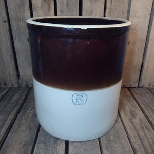 May include: A vintage brown and white stoneware crock with a dark brown upper section and a white lower section. The crock features a blue number 5 in a heart-shaped design. The rim is white.