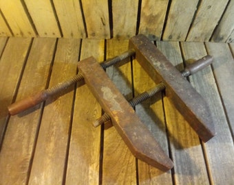 May include: A vintage wooden clamp with two adjustable screws and a wooden handle. The clamp is made of dark brown wood and has a rustic appearance.