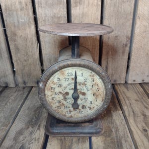 May include: An antique Columbia Family Scale with a round face and a circular dial. The scale has a rusty, aged appearance, with visible wear and tear. The dial features numbers and the words "Columbia Family Scale" and "Warranted". The scale is made of metal.