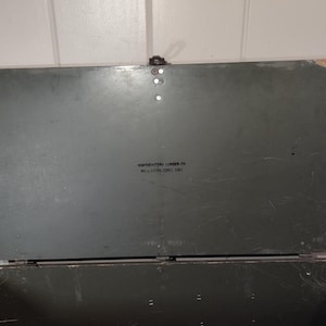 May include: A dark green wooden storage box with a hinged lid. The lid has a label that reads "Northeastern Lumber Co. Mill & Distributing Corp. 1953."