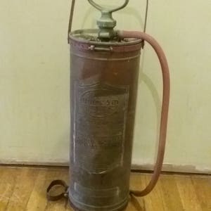May include: An antique brass fire extinguisher with a red hose and a handle. The extinguisher has a label that reads "The Quick Aid Fire Extinguisher".