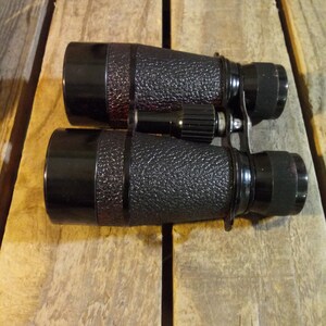 May include: Black binoculars with a textured rubber exterior. The binoculars have a central focus knob and a strap.