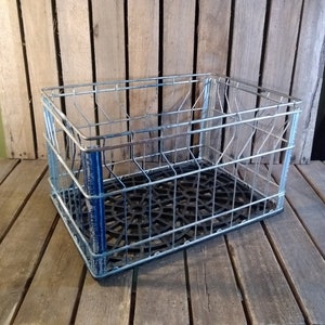 May include: A silver metal wire crate with a black plastic bottom. The crate is empty and sitting on a wooden surface.