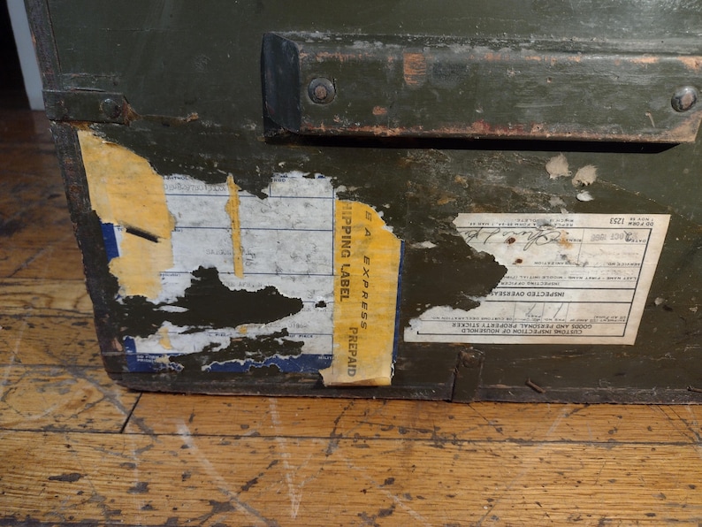 May include: A green wooden box with a black metal handle and a yellow label that says "Express Prepaid Shipping Label". The box has a label with the text "Inspected Overseas Goods and Personal Property Shipped from Homeward", "20.12.1921", and "30.4.1921".