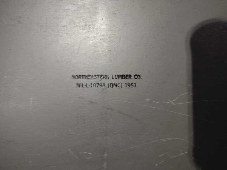 May include: A gray metal box with the text "NORTHEASTERN LUMBER CO. MIL-L-10798 (QMC) 1951" printed on the front.