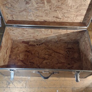 May include: An empty, open, wooden storage trunk with silver metal accents and a black handle. The inside of the trunk is lined with plywood.