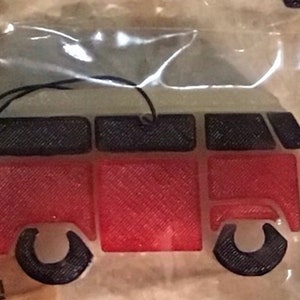 May include: A red, black, and white camper van-shaped ornament with a black string for hanging. The van has a red body, black tires and roof, and a white top. The ornament is in a clear plastic package.