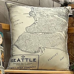 May include: Square pillow featuring a vintage map of Seattle, Washington, in black and white. The pillow includes the text "Seattle" and "Puget Sound." The map shows a detailed view of the city and surrounding areas.