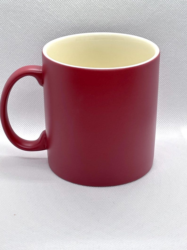 Puede incluir: Una taza cil&iacute;ndrica de cer&aacute;mica con un acabado exterior rojo oscuro mate y un interior liso de color crema. La taza cuenta con un asa roja a juego en forma de C en el lado izquierdo, ofreciendo un dise&ntilde;o sencillo y funcional para bebidas.
