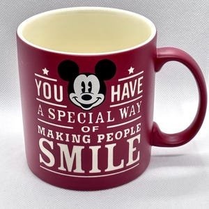 Puede incluir: Una taza de cer&aacute;mica color burdeos mate con interior crema y asa en el lado derecho. El frente presenta un gr&aacute;fico en blanco y negro de la cabeza de Mickey Mouse sobre el texto blanco: YOU HAVE A SPECIAL WAY OF MAKING PEOPLE SMILE.