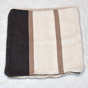 Puede incluir: Una funda de cojín cuadrada con un diseño de bloques de color que presenta un panel ancho de color gris carbón oscuro a la izquierda, seguido de una raya fina de color tostado, un panel ancho crema y una raya fina tostada final a la derecha.