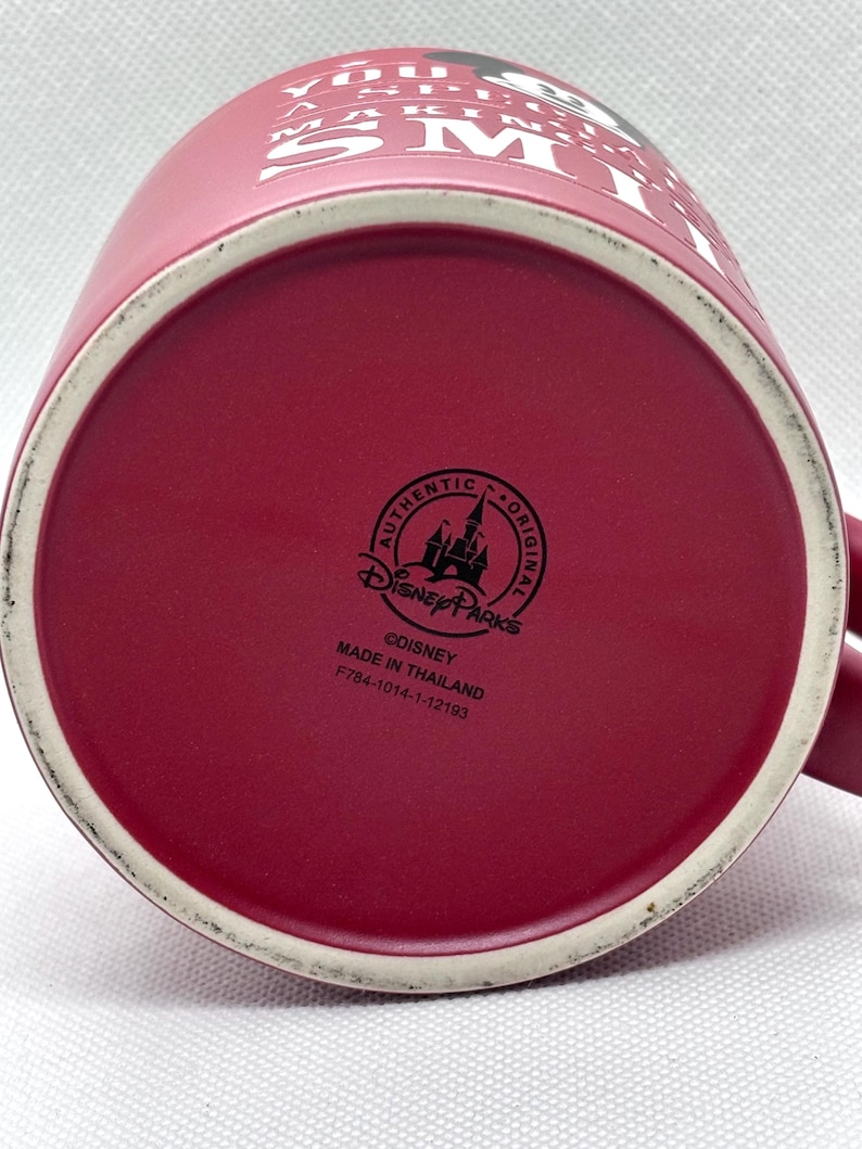 Puede incluir: Una taza de cer&aacute;mica de color rosa oscuro con texto blanco en el lateral que dice YOU A SPECIAL MAKING SMILE. La base presenta un logotipo negro de Disney Parks, el texto AUTHENTIC ORIGINAL, &copy;DISNEY, MADE IN THAILAND y el c&oacute;digo F784-1014-1-12193.
