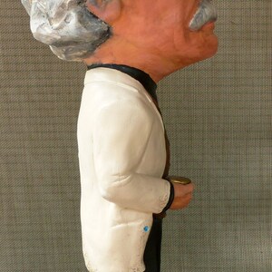 May include: A white ceramic figurine of a person wearing a white jacket and black pants. The figurine is standing on a brown base with the words 'The Farm' written on it.