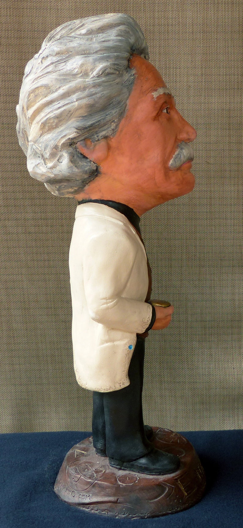 May include: A white ceramic figurine of a person wearing a white jacket and black pants. The figurine is standing on a brown base with the words 'The Farm' written on it.