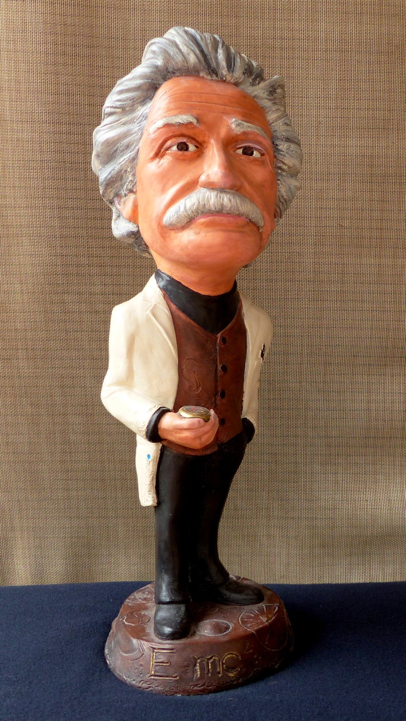 May include: A figurine of a person with white hair and a brown mustache wearing a white jacket, brown vest, and black pants. The figurine is standing on a brown base with the word 'Emc' inscribed on it.