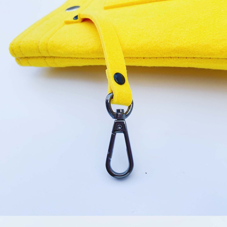 May include: Bright yellow felt clutch with a matching strap and a gunmetal-colored clasp. The clutch has a rectangular shape and a simple design. The strap is attached with black rivets. The clasp is a swivel type.
