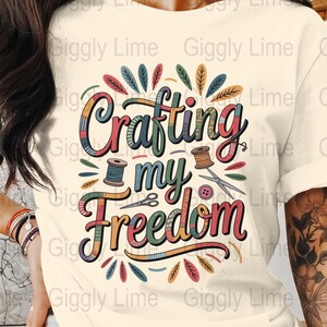 Könnte beinhalten: Cremefarbenes T-Shirt mit dem Text "Crafting my Freedom" in einem farbenfrohen, verspielten Design. Das Design beinhaltet Garnrollen, Scheren und einen Knopf, was auf ein Bastelthema hindeutet.