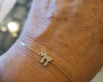 Peut inclure: Un bracelet en or fin orné d'un symbole « Chai » serti de petits brillants étincelants. Le bracelet est fin et élégant, avec un design de chaîne simple. Le symbole Chai, un mot hébreu, signifie « vie ».