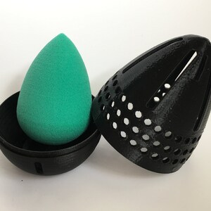 May include: A black, egg-shaped makeup sponge holder with a green sponge inside. The holder has a mesh design and a small opening on the side.
