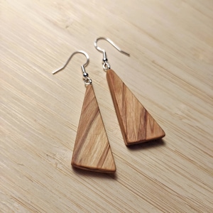Może przedstawiać: Para drewnianych kolczyków w kształcie trójkąta z naturalnym wzorem słojów drewna i srebrnymi haczykami.