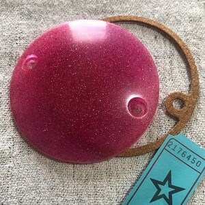 以下が含まれることがあります： ピンクのグリッターレジンディスク、茶色の革紐、星と番号2176450が書かれた青いチケット