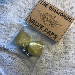 May include: Two yellow glitter diamond-shaped valve stem caps in a clear plastic bag with a brown card that says "The Diamonds Valve Caps".
