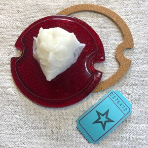 May include: A red glass lens with a white, textured, round object in the centre. A brown cork gasket is in the background. A blue ticket with a white star and the number 2176472 is in the foreground.