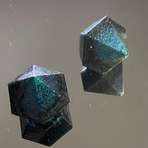 May include: Two black and green geometric resin dice with a glittery finish.