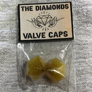 May include: Two gold glitter valve caps in a clear plastic bag with a label that reads "The Diamonds Valve Caps".