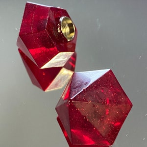 Può includere: Due tappi per bottiglia in vetro rosso, sfaccettati e geometrici. Un tappo ha una parte superiore filettata dorata.