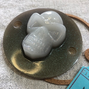 Peut inclure: Une décoration en résine en forme de crâne blanc pailleté sur un fond vert pailleté. Le crâne est en trois dimensions et présente un design détaillé.