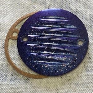 Può includere: Un coperchio motore per moto rotondo, di colore viola e oro glitterato, con un design a coste. Il coperchio ha una guarnizione in gomma marrone.