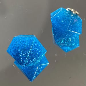 May include: Two blue glitter resin geometric shapes with a faceted design.