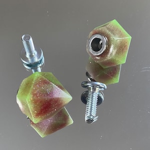 Peut inclure: Deux boutons en résine verte et rouge avec une vis et une rondelle argentées. Les boutons ont une finition mouchetée et scintillante.