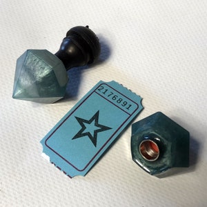 May include: Two teal blue wax seal stamps with a wooden handle and a ticket with the number 2176891 and a black star.
