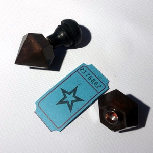 May include: A set of two vintage-style wax seals with a star-shaped ticket and the number 2176862. The seals are made of dark brown metal and have a hexagonal shape. One seal has a black knob on top.