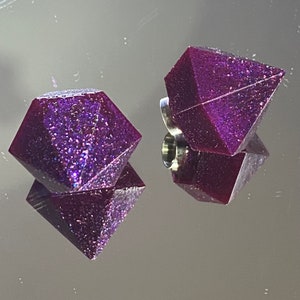 May include: Two purple diamond-shaped resin charms with glitter embedded in the resin. The charms have a silver loop for attaching to a necklace or bracelet.