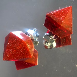 Peut inclure: Deux pièces décoratives de forme diamant rouge avec une base en métal argenté. Les pièces ont une finition brillante et scintillante.