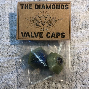 May include: Two green and blue glitter valve caps in a clear plastic bag with a brown paper tag that reads "THE DIAMONDS VALVE CAPS" with a diamond and two birds.