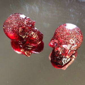 Peut inclure: Deux figurines de crâne en verre rouge avec une finition scintillante. Les crânes sont orientés dans des directions différentes.