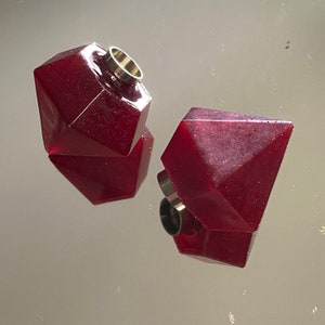 Puede incluir: Dos tapones de botella de resina roja geométrica facetada con tapas de metal plateado.