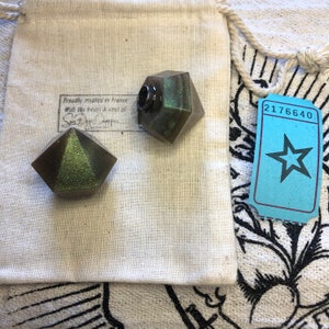 May include: Two small, geometric, green and silver bottle stoppers in a white fabric bag. The bag has a label that reads "Proudly created in France with the heart & soul of Santa Barbara Camper".