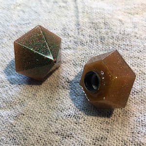 Può includere: Due tappi per bottiglia di forma geometrica, di colore marrone e glitterati. Un tappo ha un'apertura filettata.