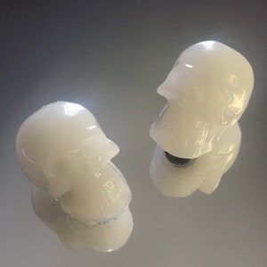 Peut inclure: Deux figurines de crâne en céramique blanche. Les crânes sont lisses et ont une finition brillante.