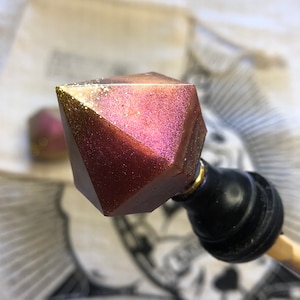 Peut inclure: Un bouchon de bouteille en résine rose et or pailletée en forme de diamant. Le bouchon est fixé à une base en métal noir et or.