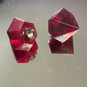 May include: Two red, faceted glass bottle stoppers with a threaded metal insert. The stoppers are shaped like a diamond.