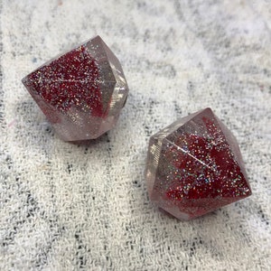 Peut inclure: Deux ornements en résine transparents, facetés, en forme de diamant avec des paillettes rouges incrustées à l'intérieur.