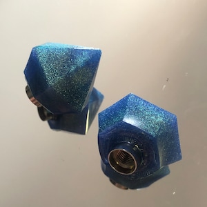 Può includere: Due tappi per bottiglia geometrici blu e scintillanti. I tappi hanno la forma di un diamante e di un esagono.